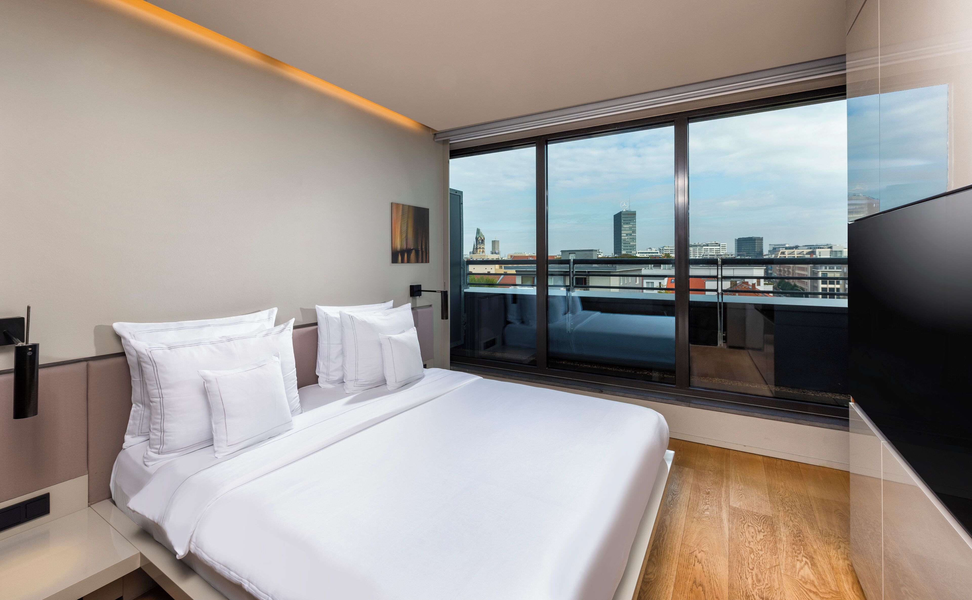 Ein modernes Hotelzimmer mit einem großen Bett, einem Fernseher und einem Balkon mit Blick auf die Stadt.