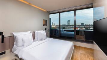 A modern hotel room with a large bed, a TV, and a balcony with a city view.