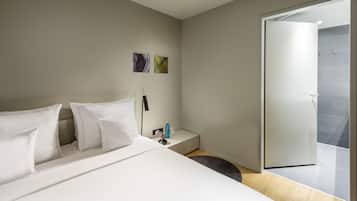 A modern hotel room with a large bed, a bedside table with a lamp, and a view of the outside through a glass door.