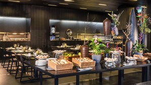 Ein reichhaltiges Buffet mit verschiedenen Speisen, darunter Brot, Gebäck und Früchte, präsentiert auf Tischen mit Stühlen.