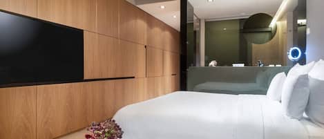 Una habitación de hotel moderna con una cama grande, un panel de pared de madera, una mesa de centro redonda con un jarrón de flores y un espejo grande con luz circular.