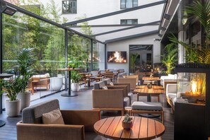 A spacious outdoor seating area with multiple tables and chairs, surrounded by large potted plants and a fire feature. - SANA Berlin Hotel (Berlin)