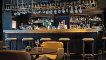 Zona de bar con varios taburetes, una barra con un bartender y una variedad de botellas y vasos.