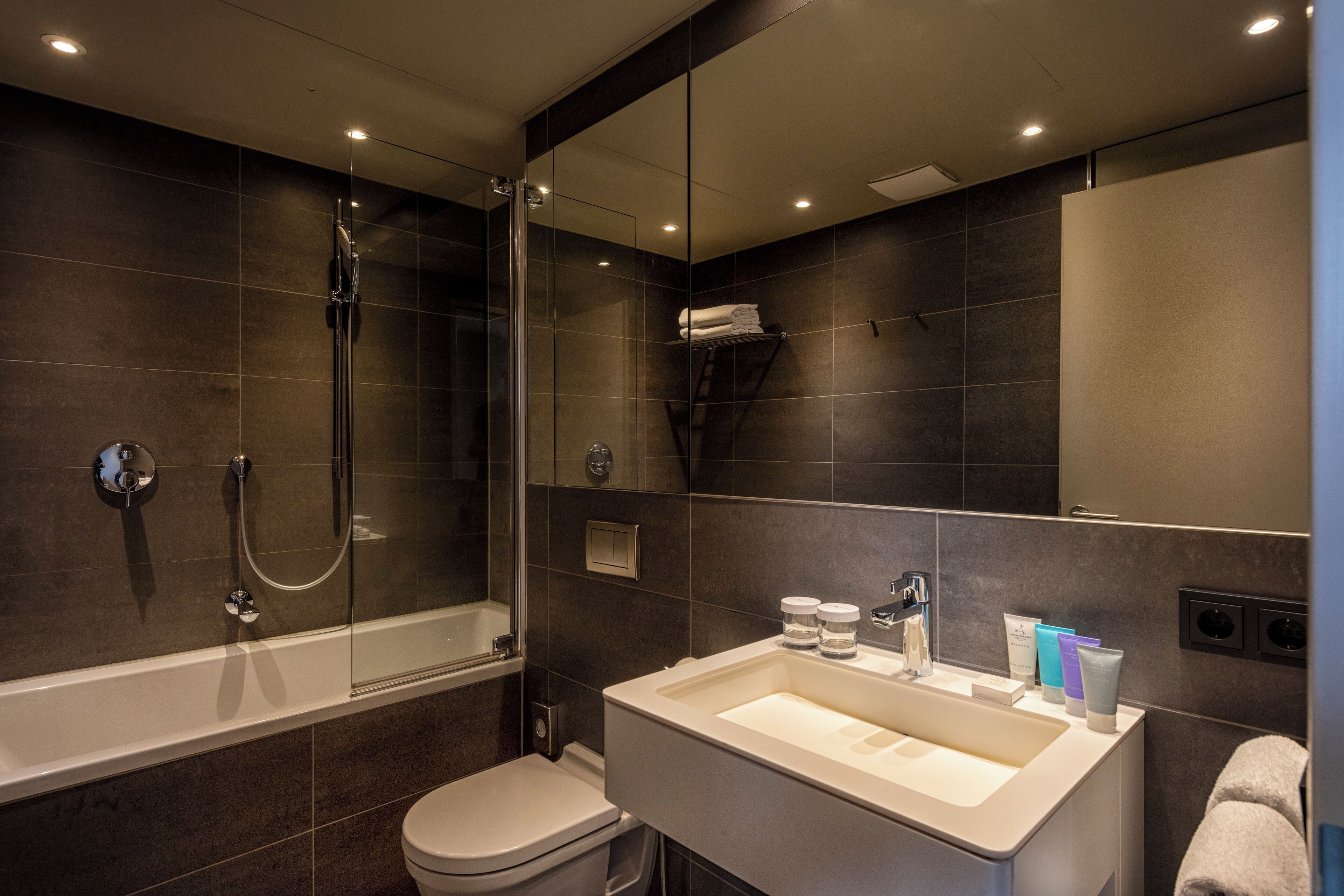 A modern bathroom with a glass-enclosed shower, a white sink with toiletries, and a large mirror.