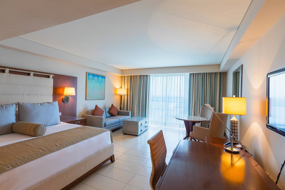 Quarto de hotel com uma cama grande, um sofá, uma mesa de jantar e vista para a cidade.