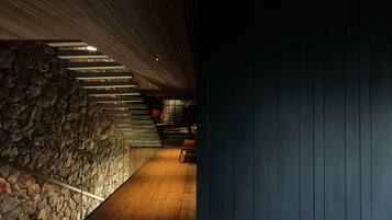 A staircase with a stone wall on one side and a dark wooden wall on the other, leading to a room with a bench and a table.