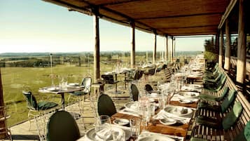 Un área de comedor al aire libre con mesas dispuestas para una comida, con vistas a un paisaje pintoresco.