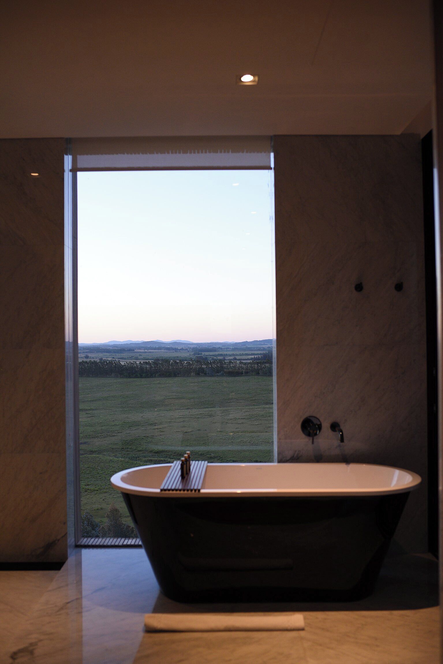 A modern bathroom with a freestanding bathtub, a large window, and a view of a grassy field.