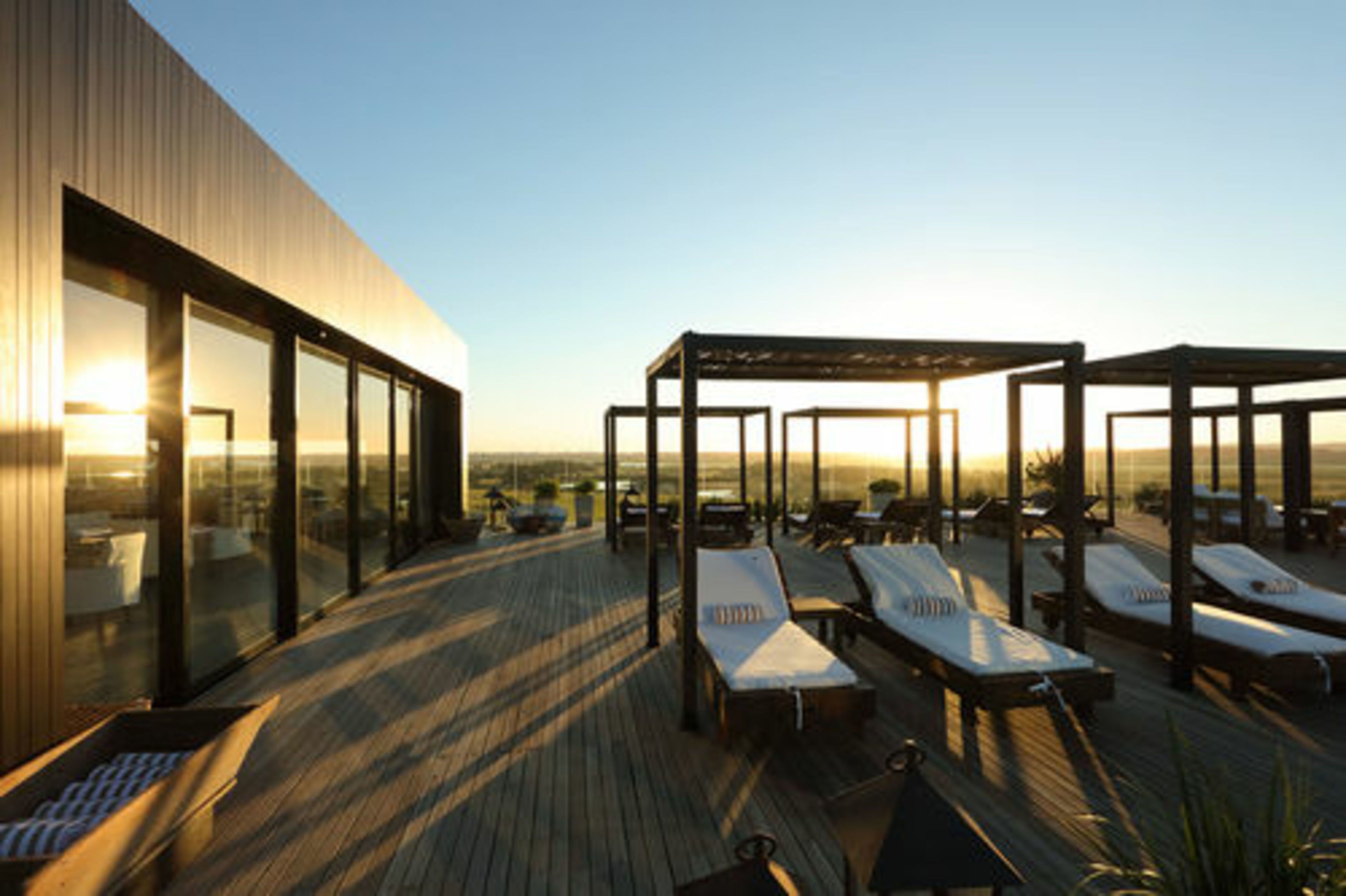 A rooftop terrace with sun loungers and a glass-enclosed area with seating.