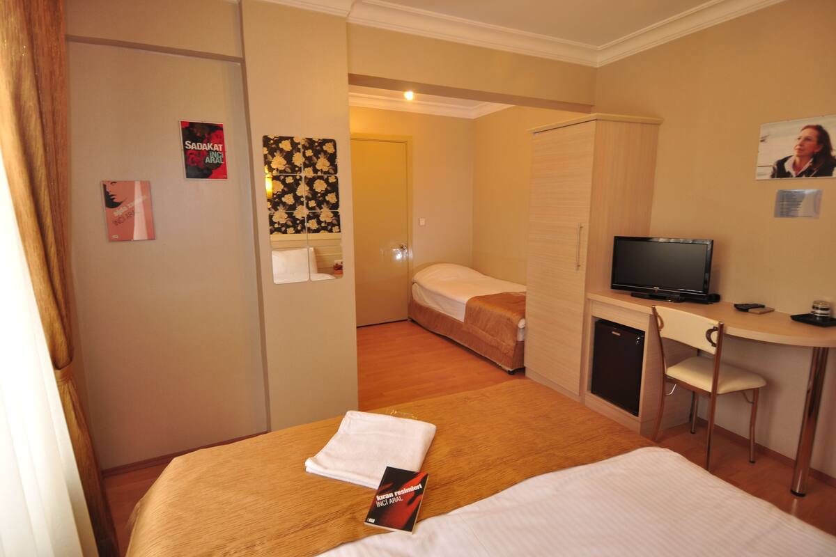 A hotel room with a bed, a desk with a TV, a small fridge, and a door leading to another room.