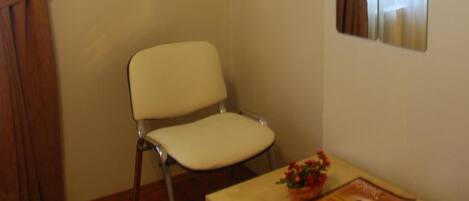 A room with a white chair, a small table with a magazine, and a window with curtains.