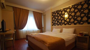 A hotel room with a large bed, a desk with a computer, and a wall-mounted light fixture. - Mini Fuar Hotel (Izmir)