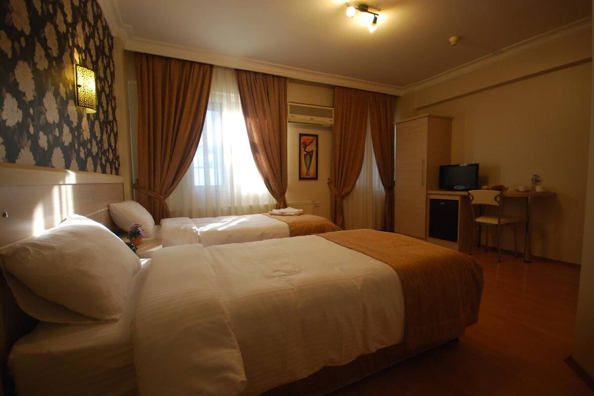 A hotel room with two beds, a desk, a television, and an air conditioning unit.