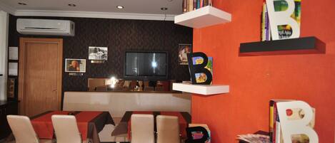 A dining area with a TV, bookshelves, and a clock on the wall.