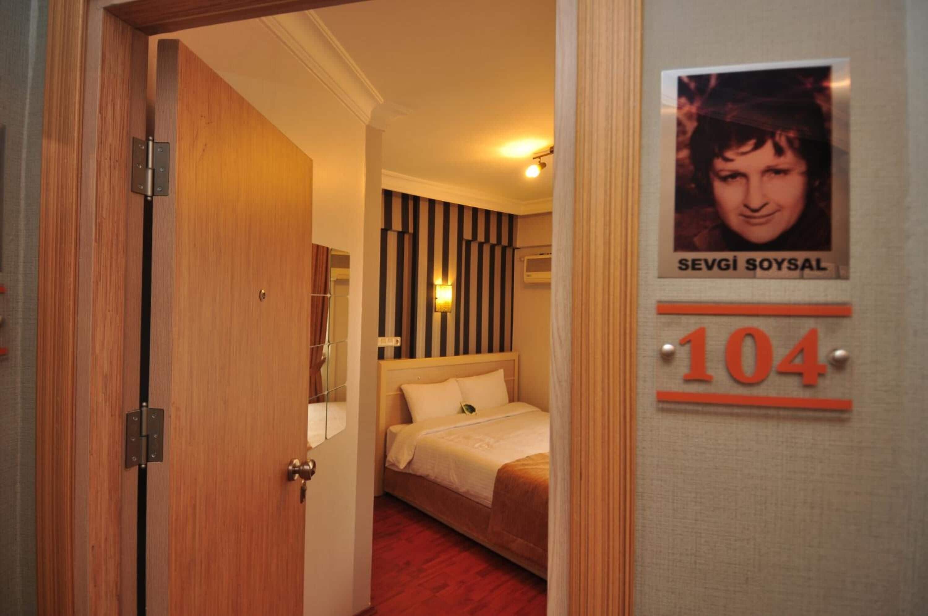 A hotel room with a bed, a striped wall, and a door with a number sign.