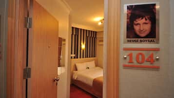 A hotel room with a bed, a striped wall, and a door with a number sign.