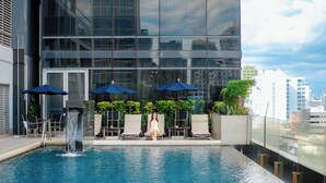 A rooftop pool with a water feature, lounge chairs, and umbrellas.