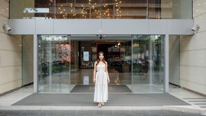 A modern building entrance with a glass facade, a visible upper floor, and a decorative light fixture.