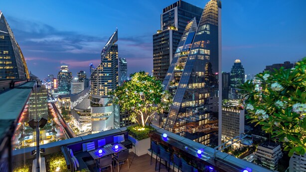A rooftop bar with a view of a cityscape at dusk, featuring modern skyscrapers and a well-lit urban environment.
