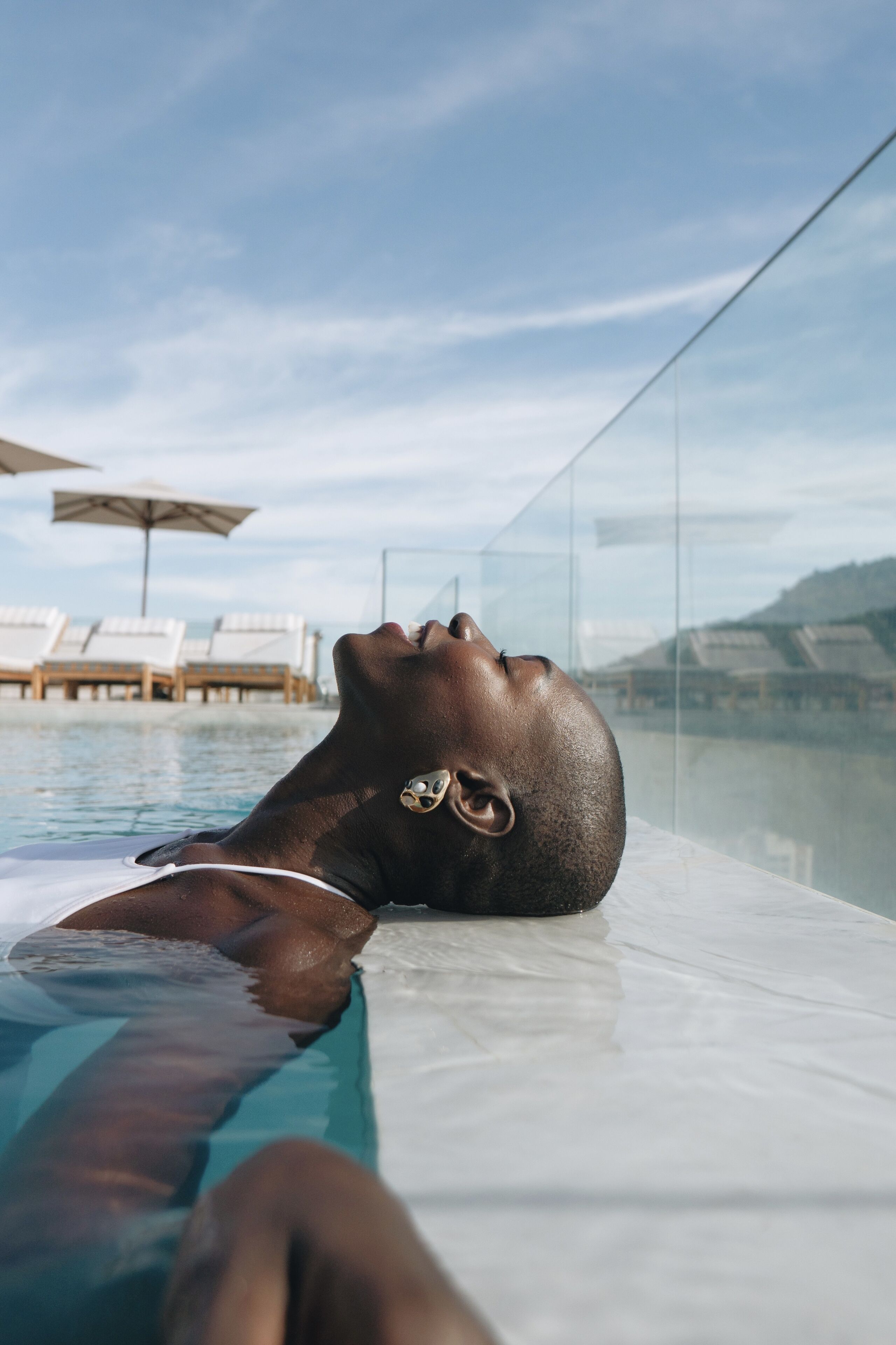 A person relaxing in a pool with lounge chairs and umbrellas in the background.
