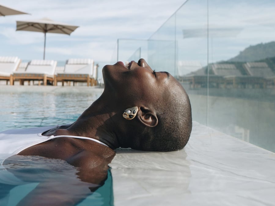 En person som kopplar av i en pool, med solstolar och parasoller i bakgrunden.