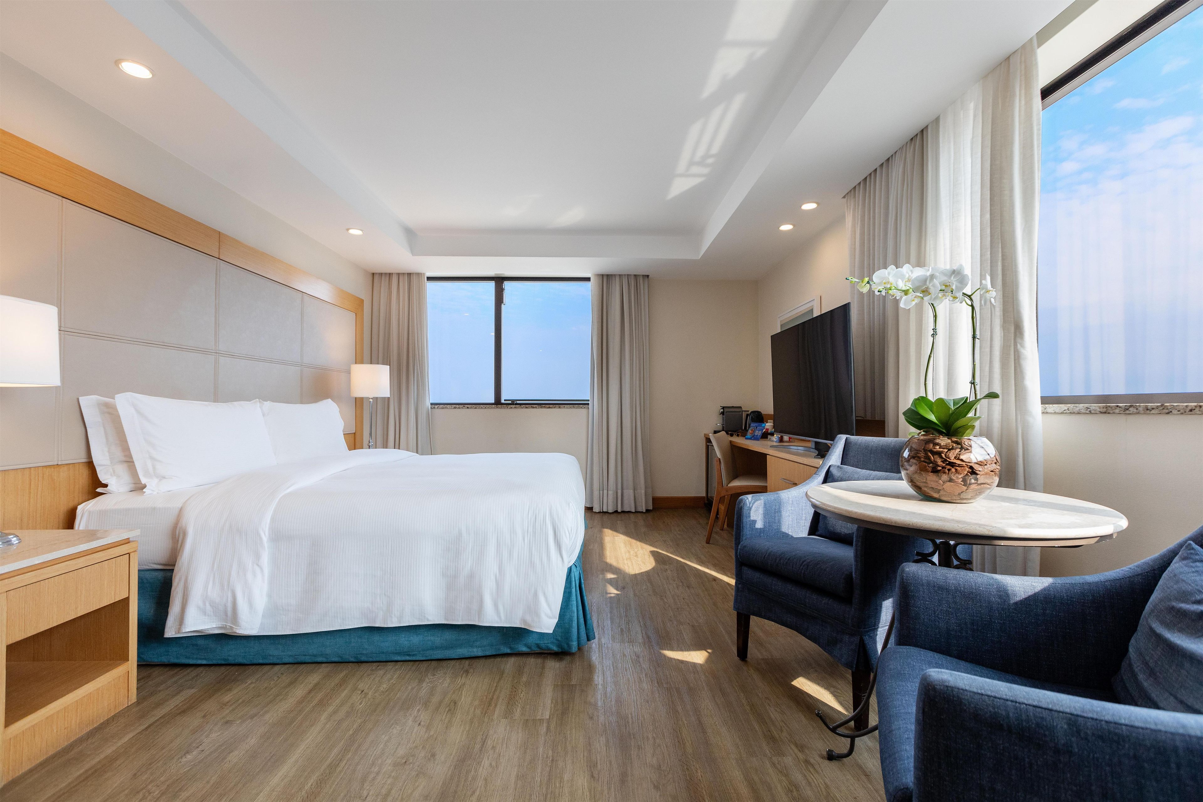 Une chambre d’hôtel avec un lit, un bureau, une chaise, une télévision et une fenêtre avec des rideaux.