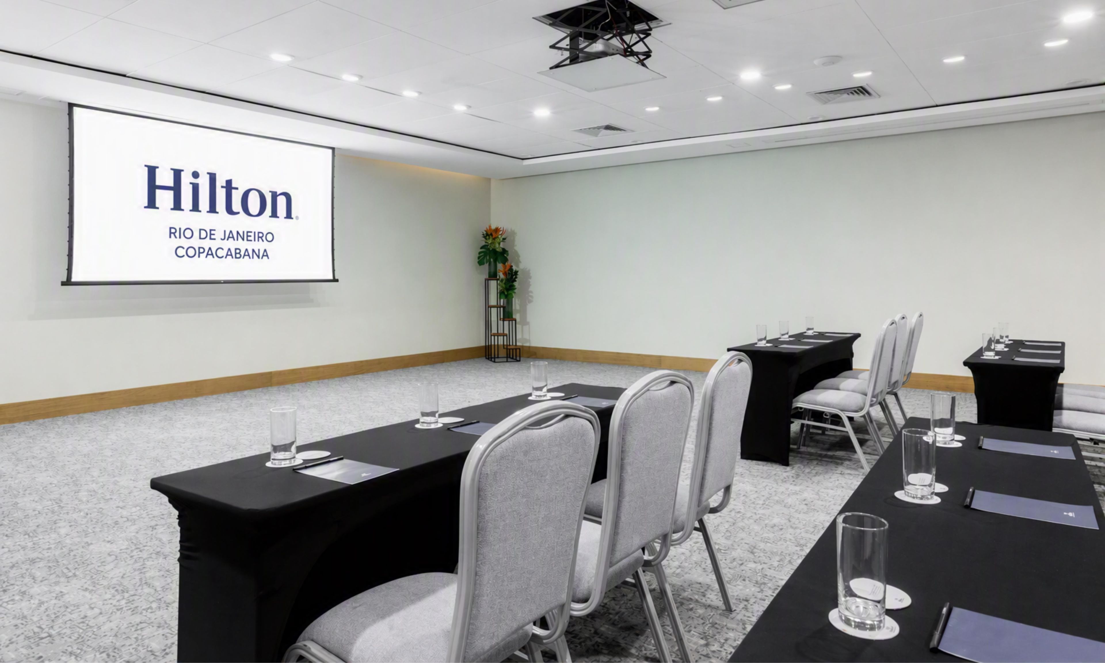 A conference room with a projector screen displaying 'Hilton Rio de Janeiro Copacabana' and a long table with chairs and nameplates.