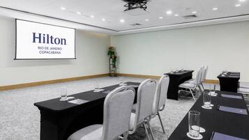 A conference room with a projector screen displaying 'Hilton Rio de Janeiro Copacabana' and a long table with chairs and nameplates.