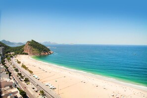 A coastal beach with a road running parallel to the shore, a mountain in the background, and a clear blue sky. - Hilton Copacabana Rio de Janeiro (Rio de Janeiro)