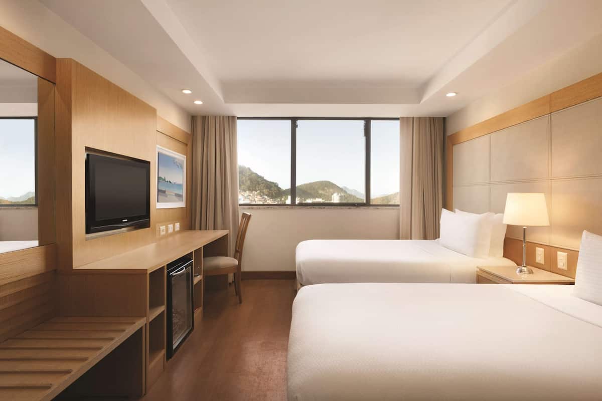 Ein Hotelzimmer mit zwei Betten, einem Fernseher, einem Schreibtisch und Blick auf Berge.