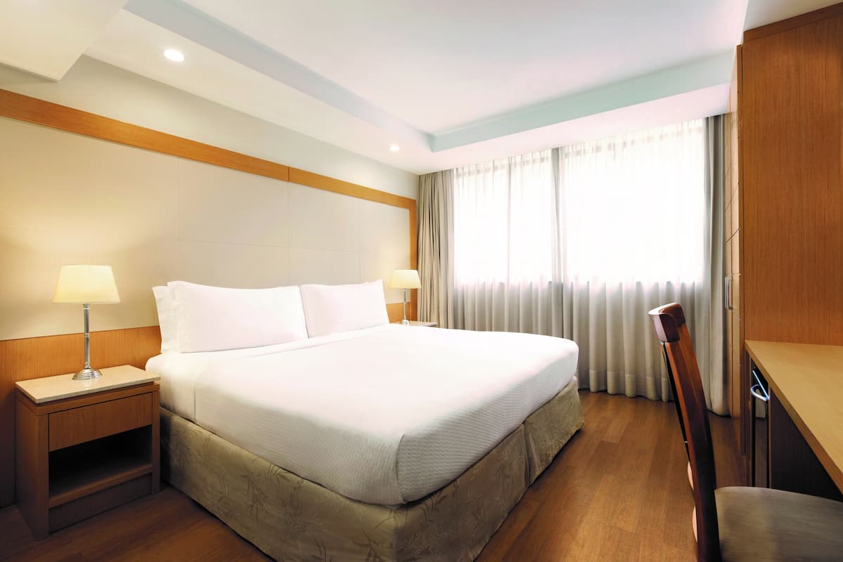 Ein Hotelzimmer mit einem großen Bett, zwei Nachttischen mit Lampen, einem Holzkopfstück, einem Schreibtisch und einem Stuhl.