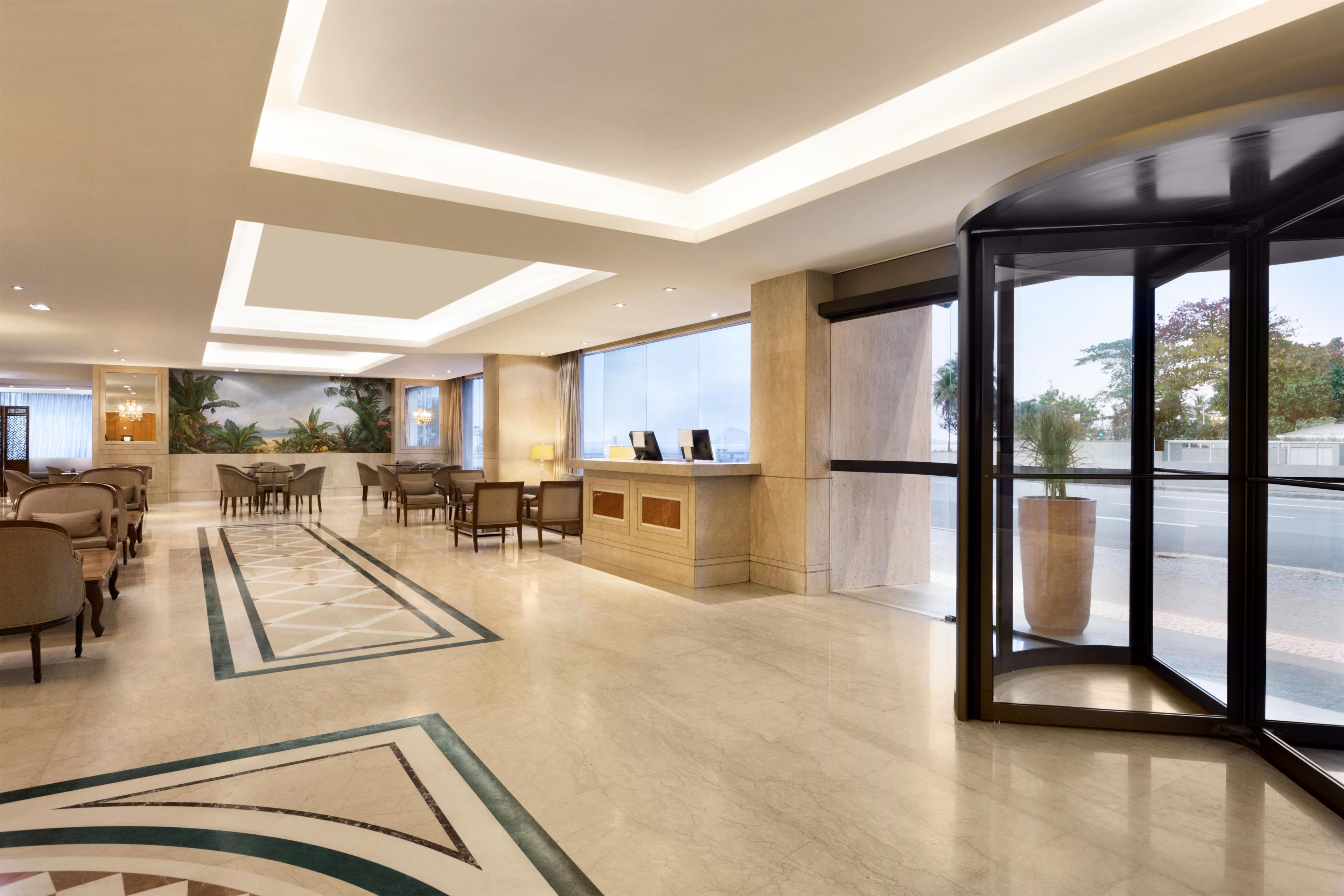 A hotel lobby with a reception desk, seating area, and large windows offering a view of the outdoors.