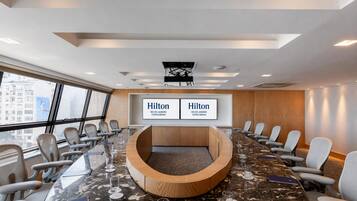 Un salón de conferencias con una larga mesa, varias sillas y una pantalla grande que muestra 'Hilton Rio de Janeiro Copacabana'.