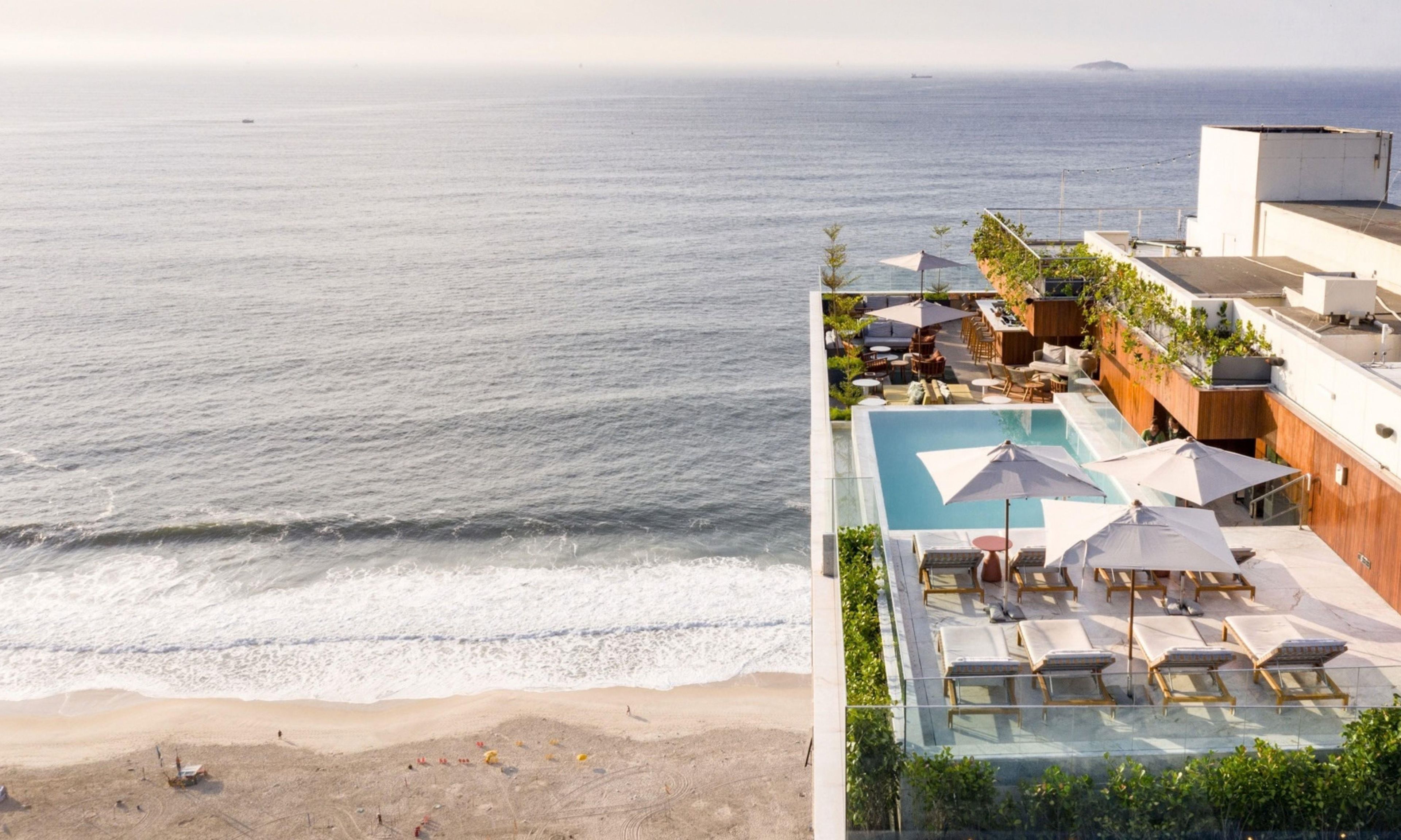 Área de piscina no terraço com espreguiçadeiras e guarda-sóis, com vista para o oceano.