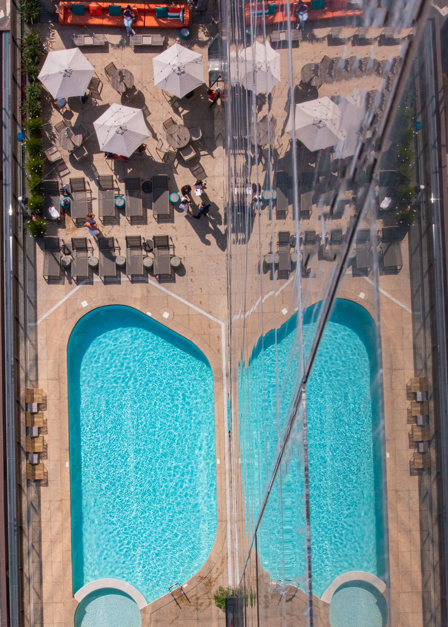 Vista aérea de una zona de piscina con sillones de descanso y sombrillas.