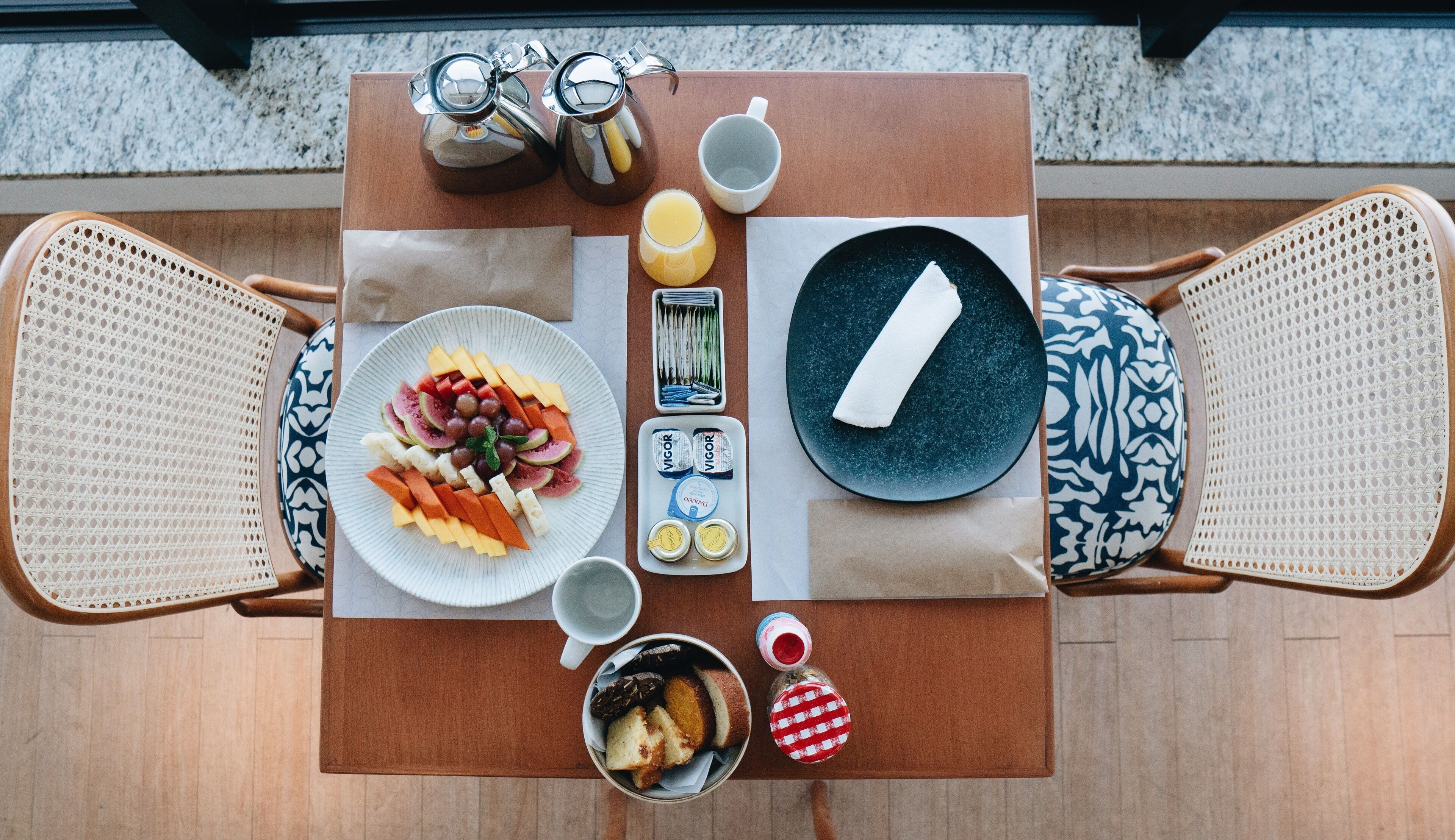 A breakfast table with plates of food, a coffee pot, a cup, and a bottle of jam.
