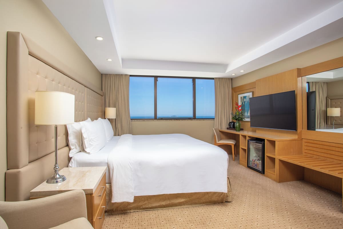 Ein Hotelzimmer mit einem großen Bett, einem Flachbildfernseher, einer Minibar und Meerblick.