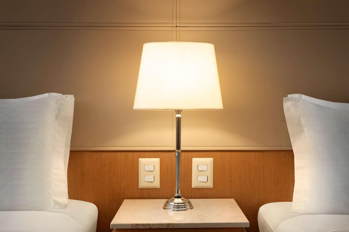 Ein Hotelzimmer mit Nachttischlampe, zwei weißen Kissen, einem Holz-Kopfteil und einem kleinen Tisch mit Lampe.
