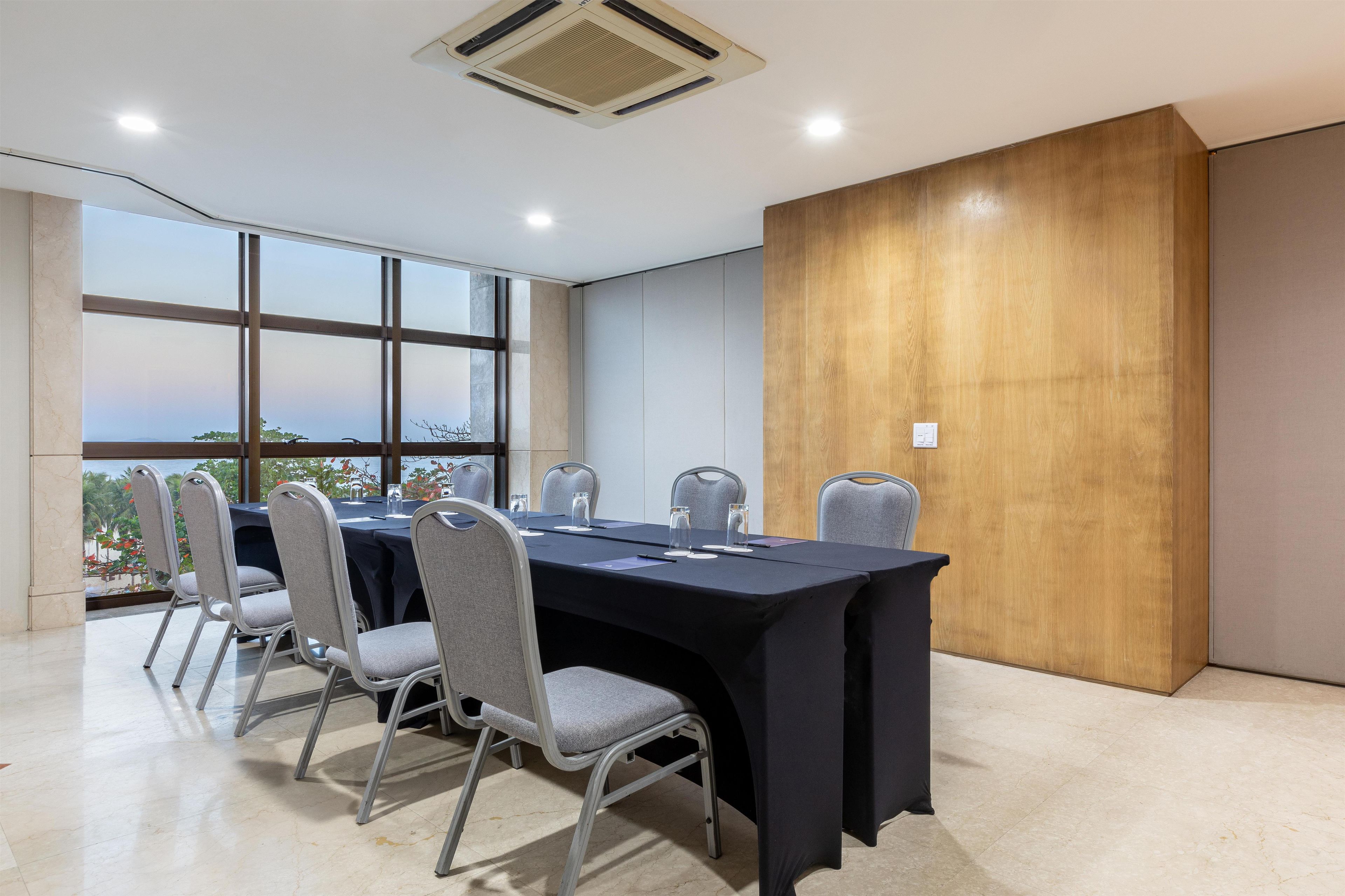 Un salón de conferencias con una larga mesa, sillas y vistas amplias a través de grandes ventanales.