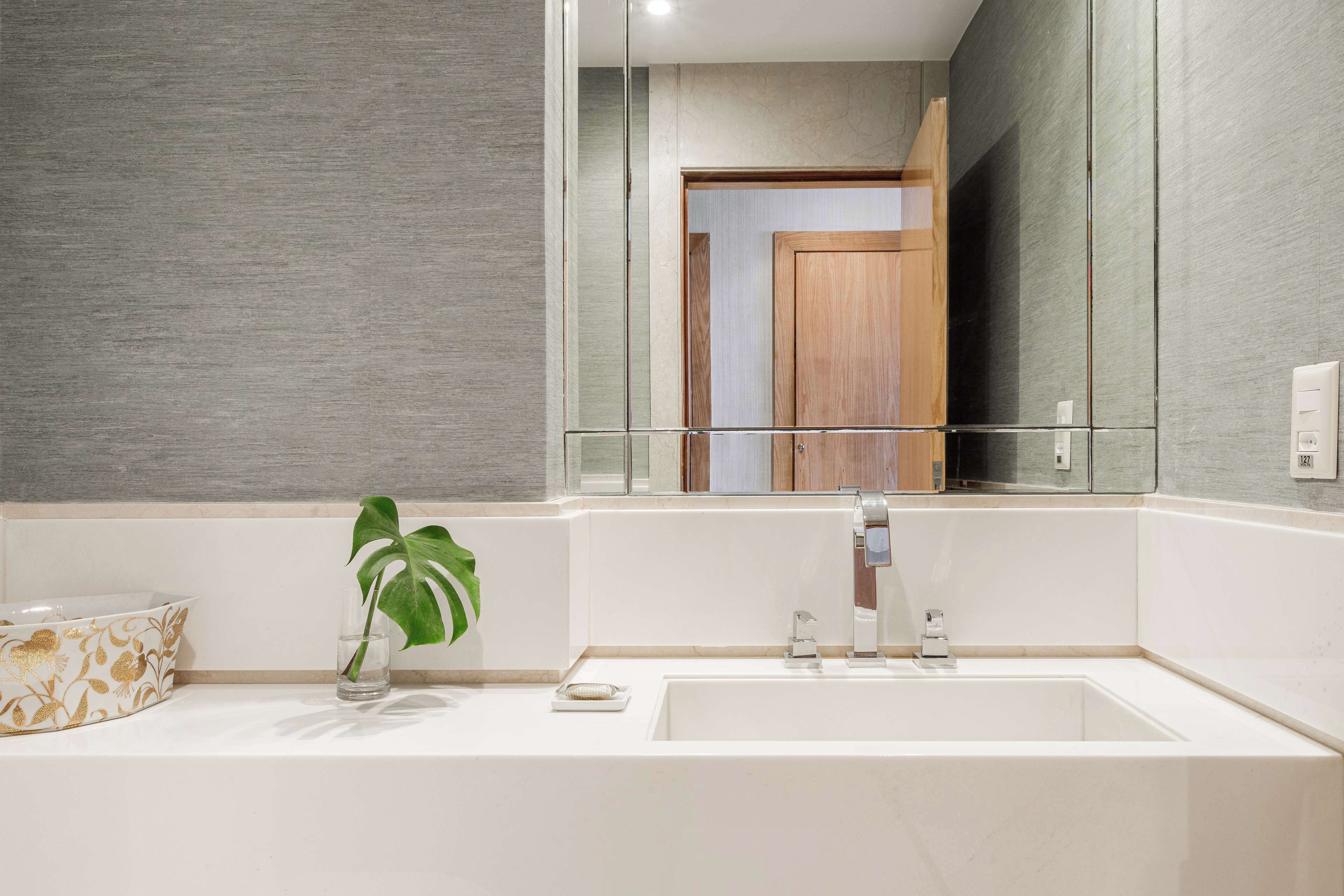 Une salle de bain moderne avec un grand miroir, un lavabo blanc et une plante.
