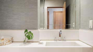 Une salle de bain moderne avec un grand miroir, un lavabo blanc et une plante.