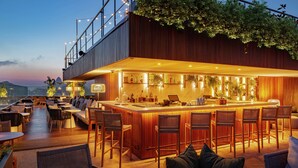 A rooftop bar with wooden bar stools, a long counter, and a view of the cityscape. - Hilton Copacabana Rio de Janeiro (Rio de Janeiro)