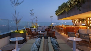 A rooftop bar with seating and a bar area, overlooking a cityscape.