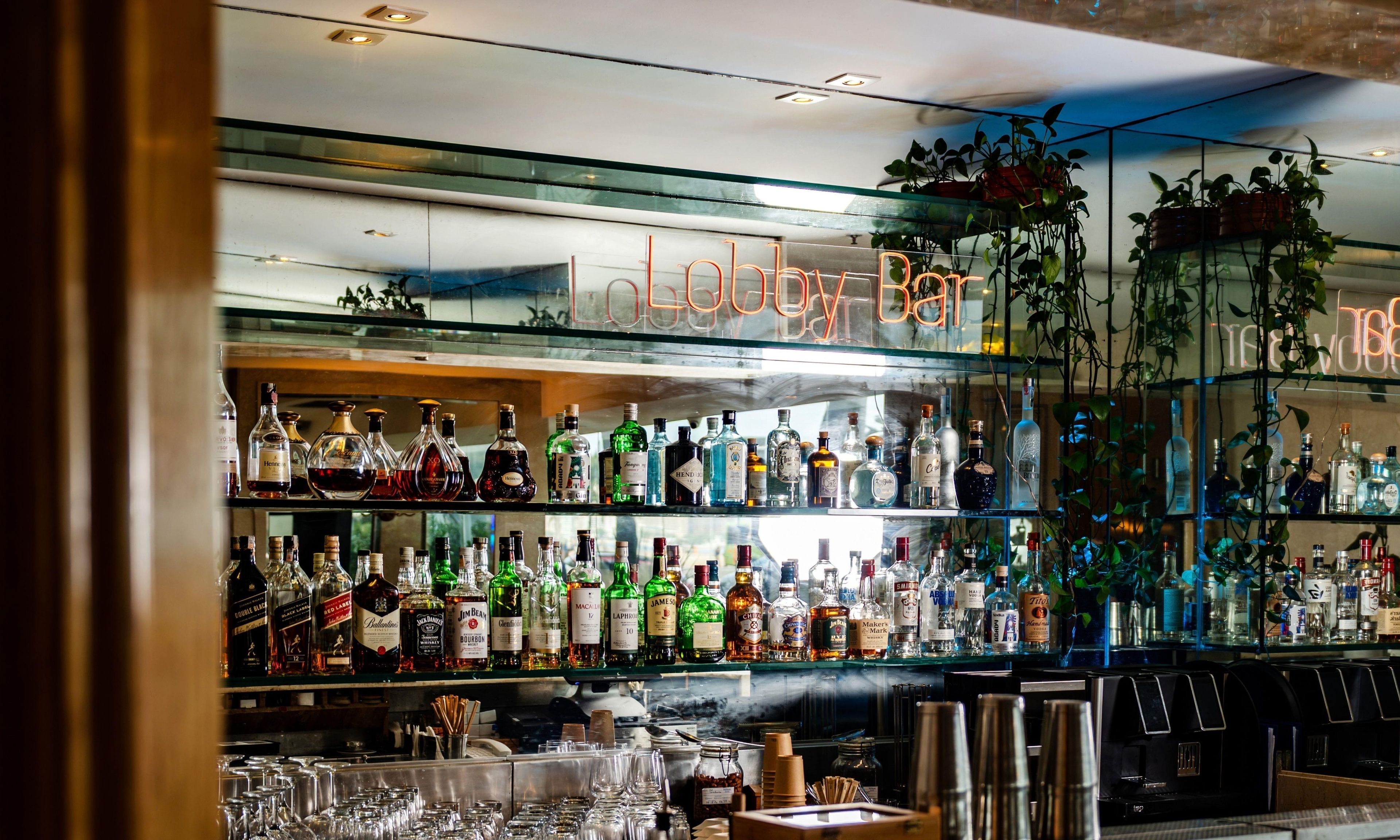 Um bar com várias prateleiras de garrafas de bebidas, copos e um letreiro de neon que diz 'Holiday Inn'.