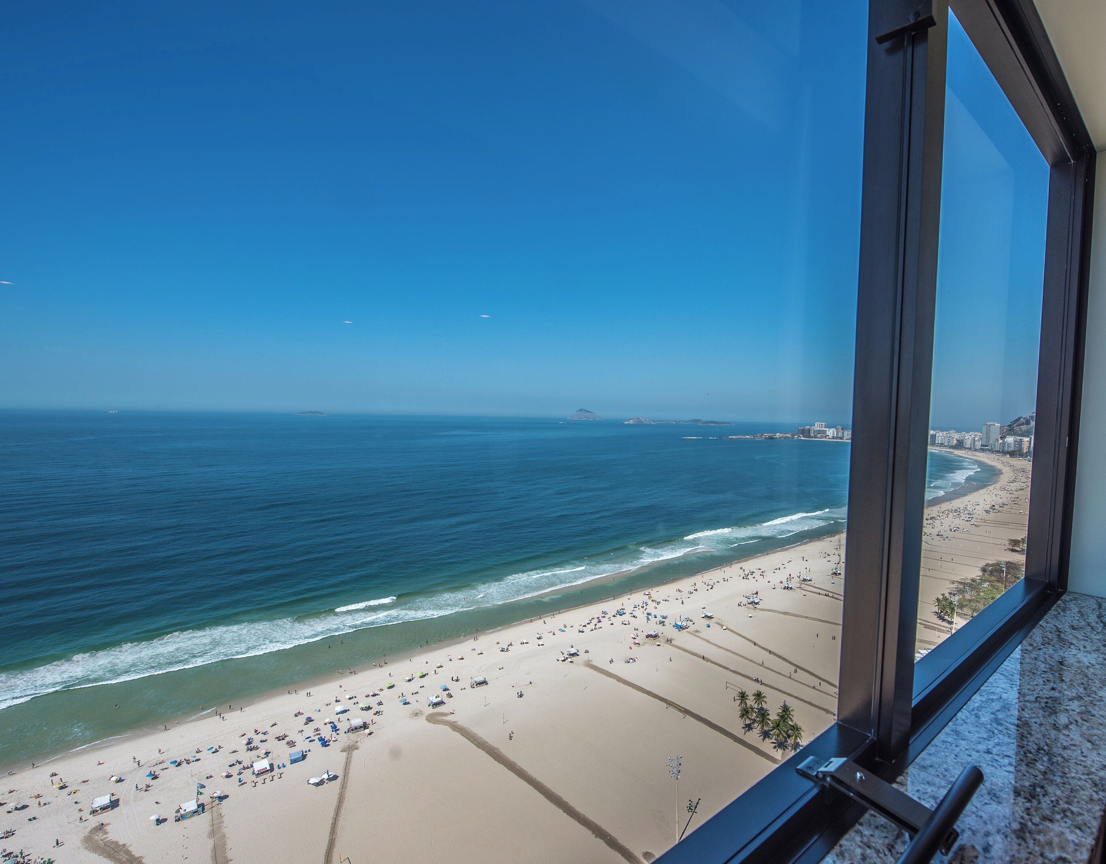 A beach view from a window overlooking a sandy beach with umbrellas and people.