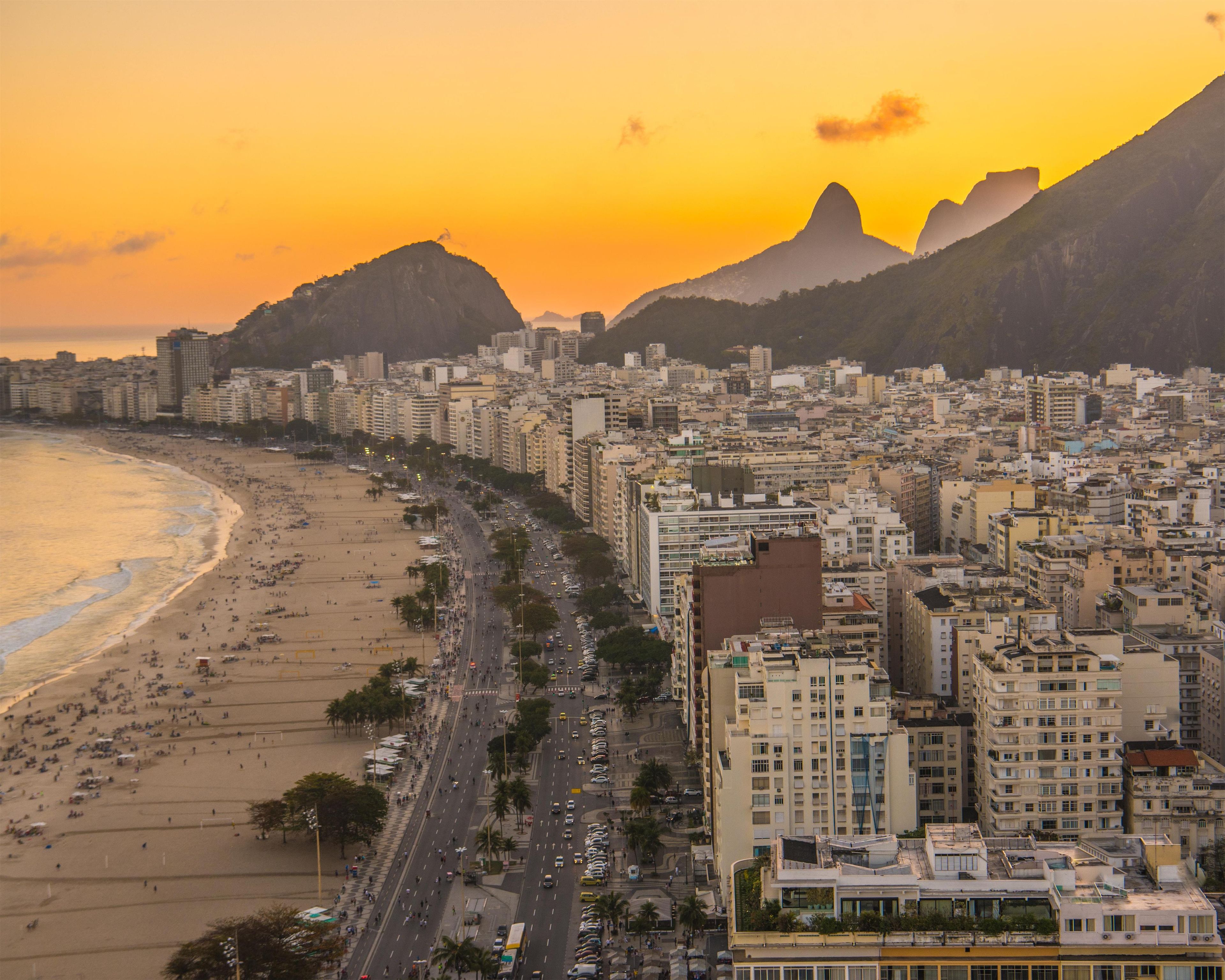 A coastal cityscape with a beach, high-rise buildings, and a prominent mountain in the background.