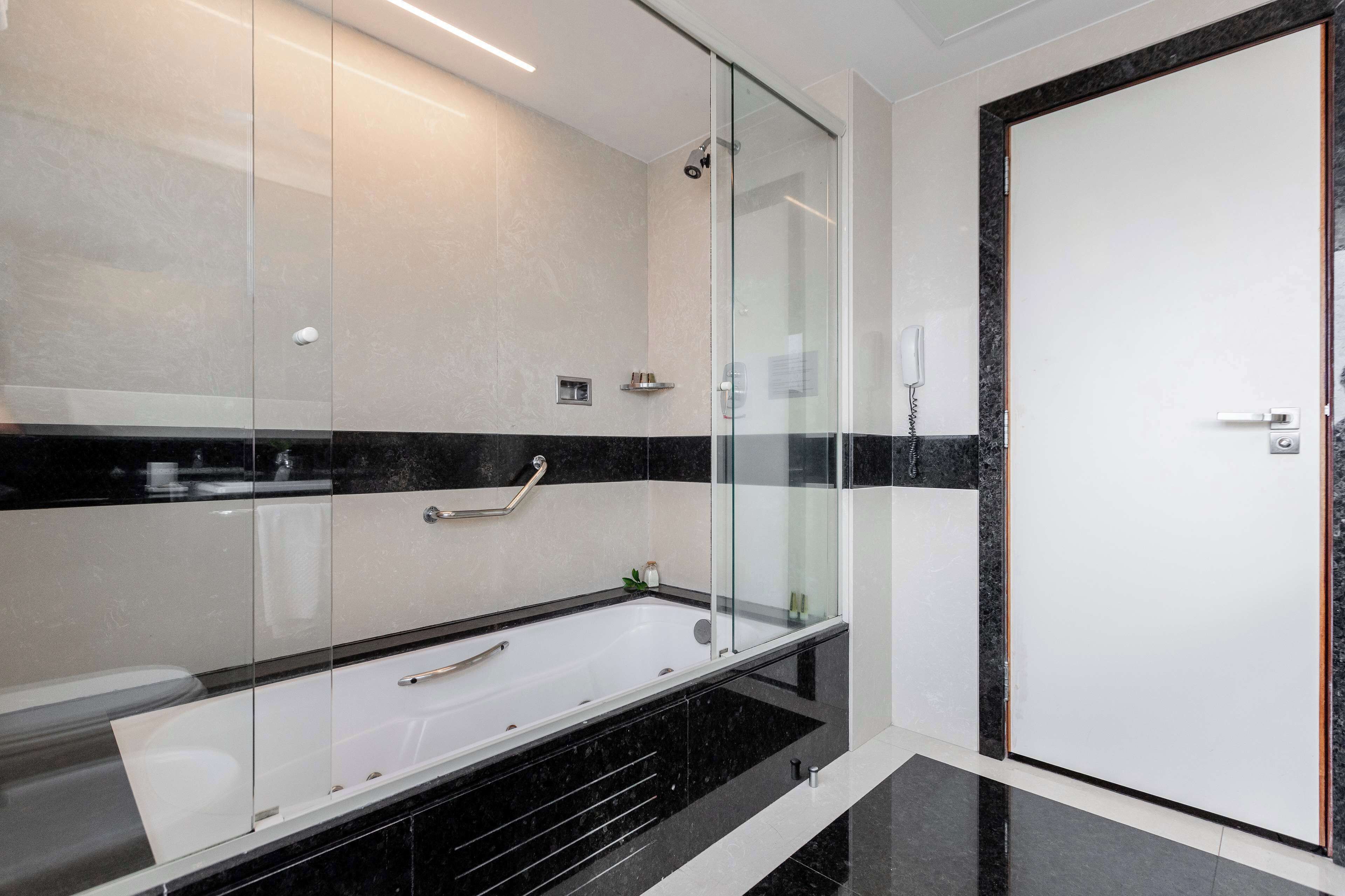 A modern bathroom with a glass-enclosed bathtub, a shower, and a white door.