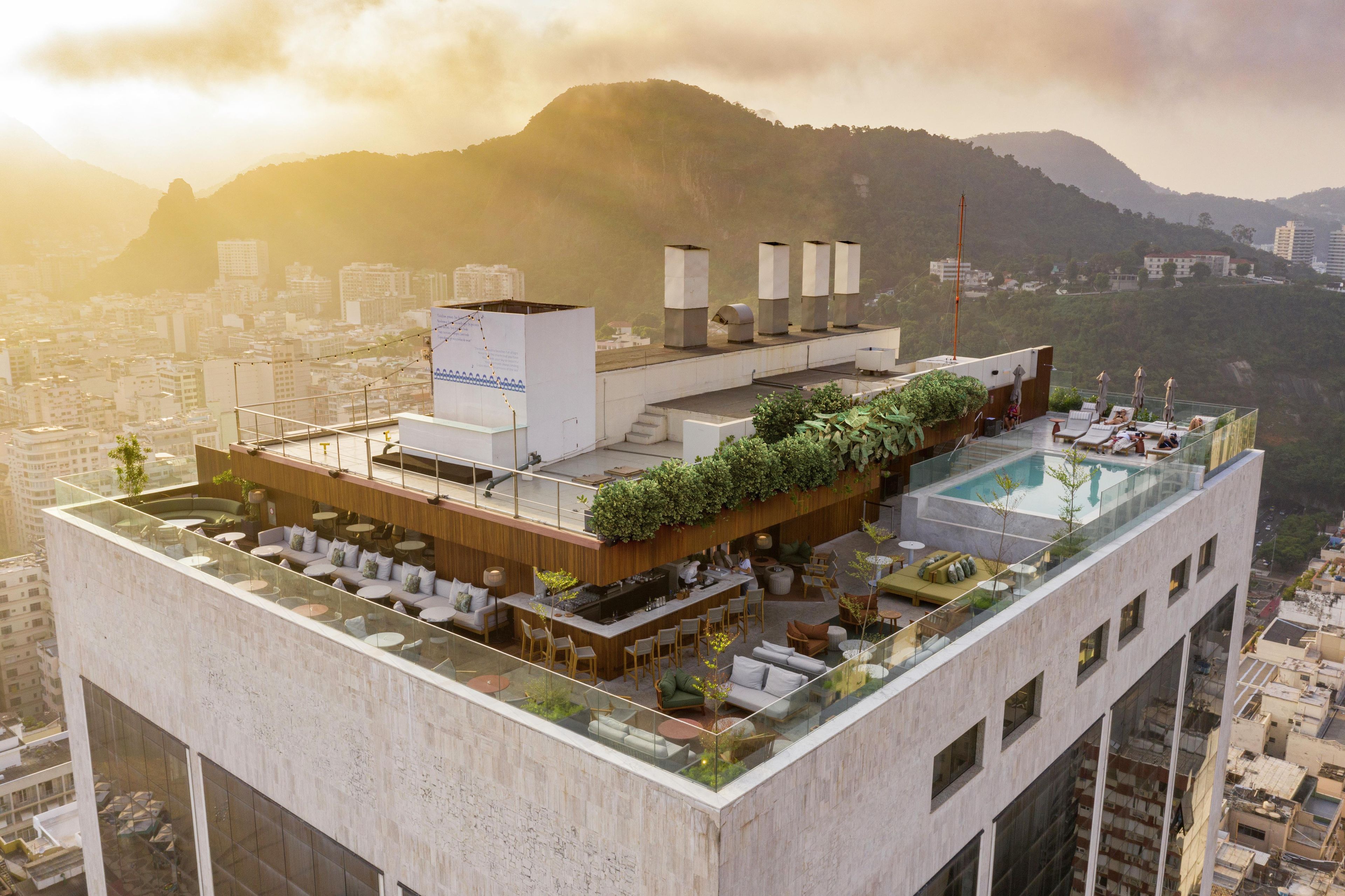 A rooftop terrace with a pool, seating areas, and a view of the cityscape and mountains.
