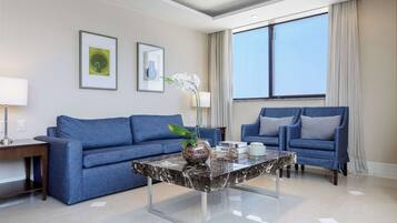 Un salon moderne avec un canapé bleu, un fauteuil assorti, une table basse en marbre et une grande fenêtre avec des rideaux.