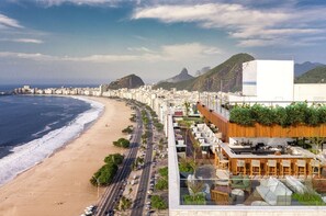 A coastal cityscape with a beach, high-rise buildings, and a restaurant with outdoor seating overlooking the ocean. - Hilton Copacabana Rio de Janeiro (Rio de Janeiro)